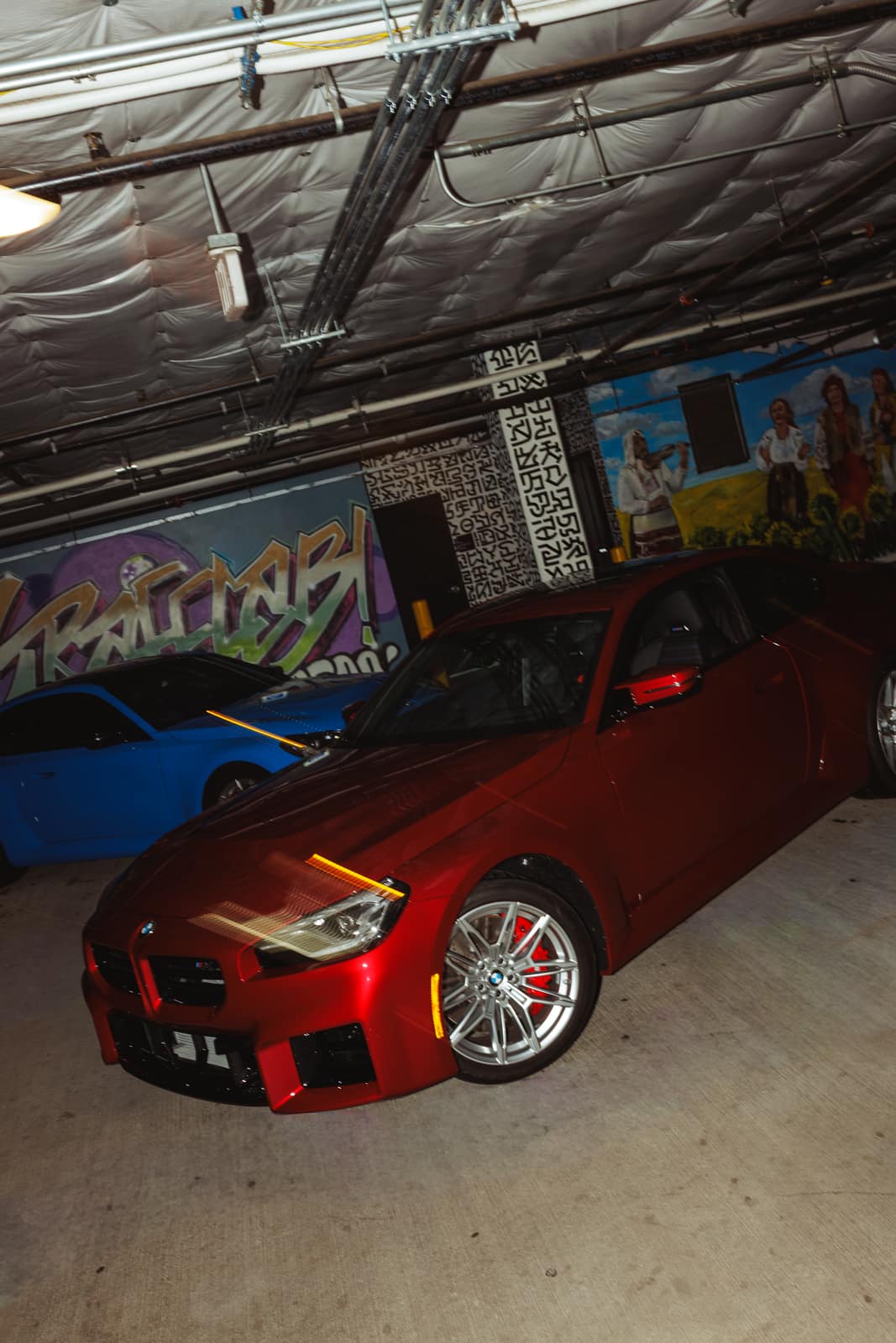 Red M2 front three-quarter in the garage, the blue car parked behind