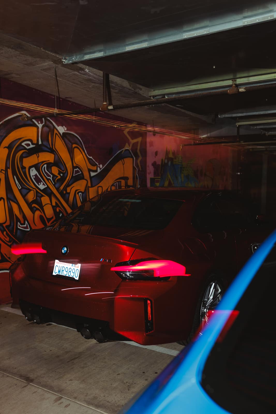 Red M2 rear three-quarter against the garage graffiti, taillights lit