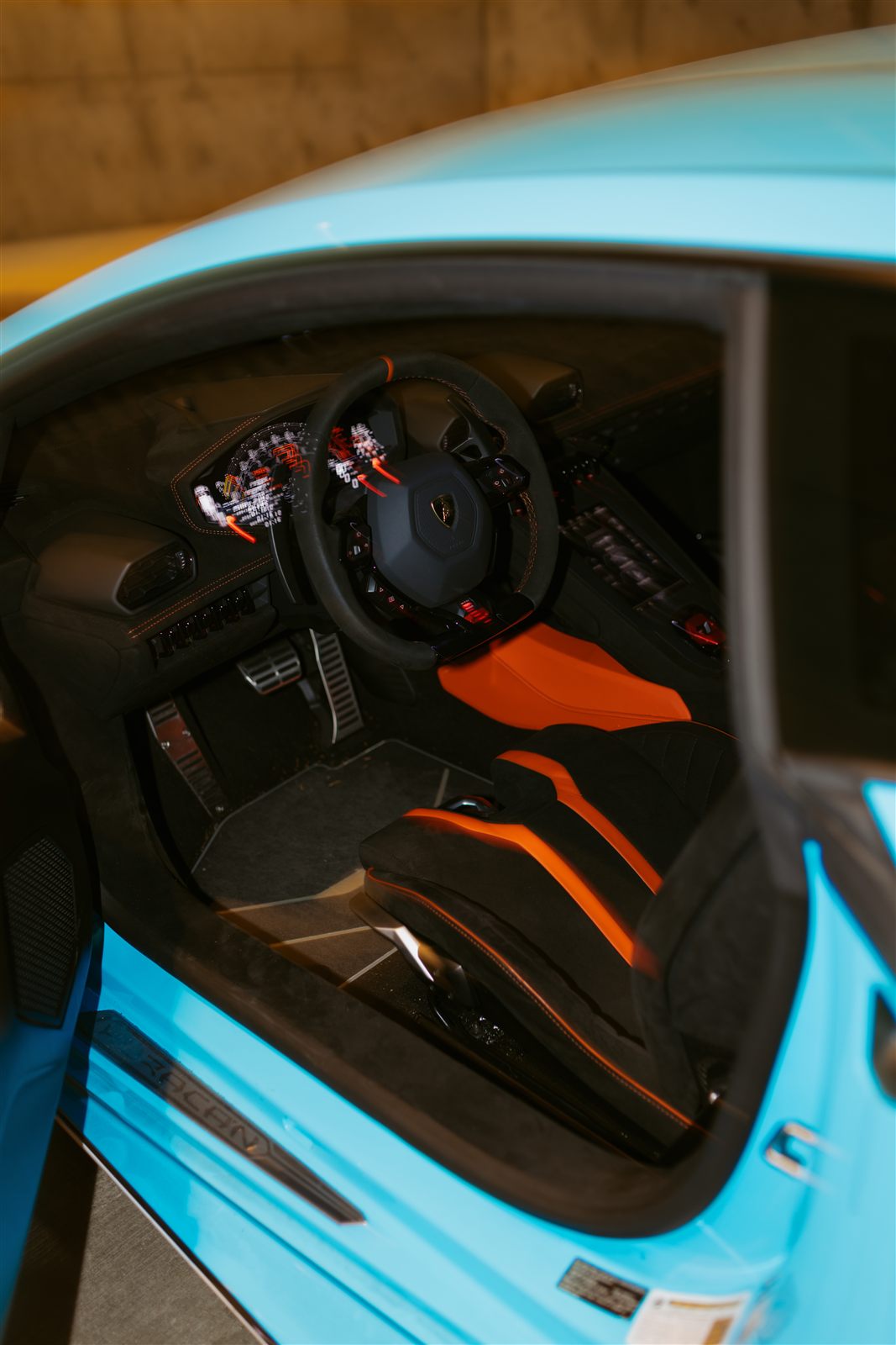 STO cockpit through the open door: wheel, digital cluster, orange racing seats